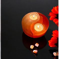 two lit candles sitting on top of a table next to some red and white flowers