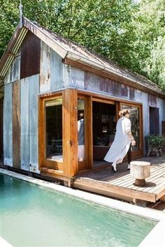 a woman walking out of a pool onto a wooden deck next to a small house