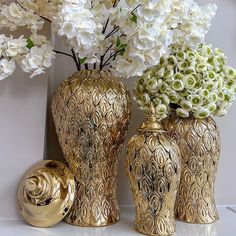 three gold vases with white flowers in them