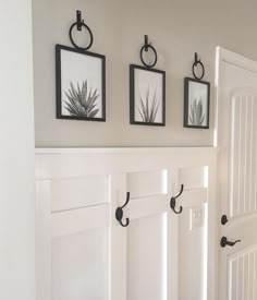 three framed pictures hang on the wall next to a white door with black handles and hooks