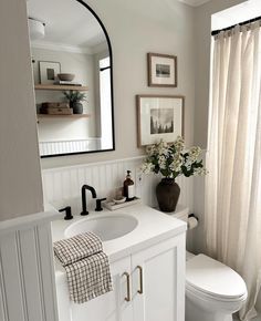 a white toilet sitting next to a sink in a bathroom under a mirror and framed pictures