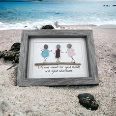 two people are standing on a beach with the ocean in the background and there is a framed artwork