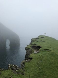 a person standing on the edge of a cliff overlooking water and cliffs in foggy weather