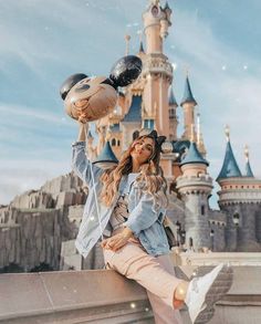 a woman sitting on top of a stone wall next to a castle with lots of balloons