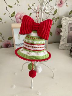 a crocheted hat with a red bow on top is sitting on a stand