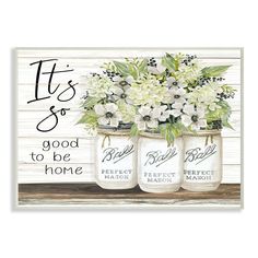 three mason jars filled with white flowers sitting on top of a wooden table next to a sign