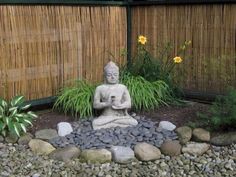 a buddha statue sitting on top of a pile of rocks next to a bamboo fence