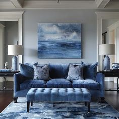 a living room with blue couches and pillows on the floor in front of a painting