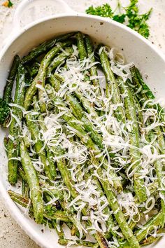 a white bowl filled with green beans covered in shredded parmesan cheese