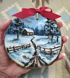 a hand holding a christmas ornament with a snowy scene on it and a red ribbon