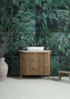 a bathroom with green marble tiles and a wooden cabinet next to a bench in front of the sink