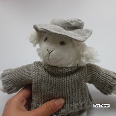 a hand holding a stuffed animal wearing a sweater and hat