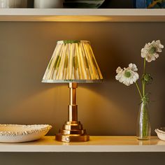 a lamp on a shelf next to a vase with flowers in it and a bowl