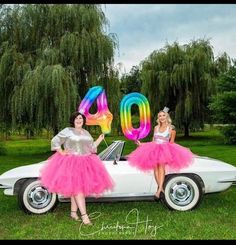 two women in dresses are sitting on a car with the number 40 written on it