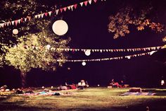 people are laying in the grass at night under lanterns and paper lanterns hanging from trees