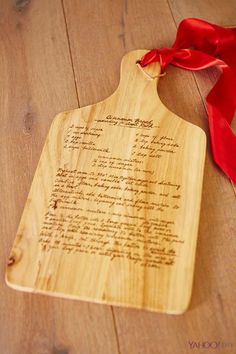 a wooden cutting board with a red ribbon around it on a wood floor next to a piece of paper