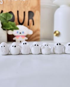 small white ghost figurines lined up in a row on a table next to a potted plant