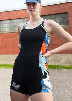 a woman standing in front of a red brick building wearing a black and blue one piece swimsuit