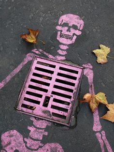 a skeleton painted on the ground next to a grate with leaves growing out of it