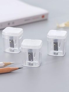 three plastic containers with pencils and sharpener on a table