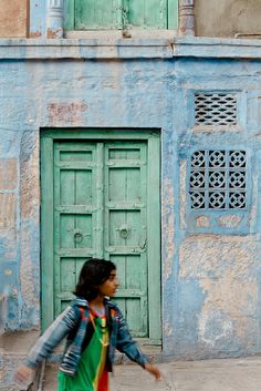 a woman walking past a blue building with green doors