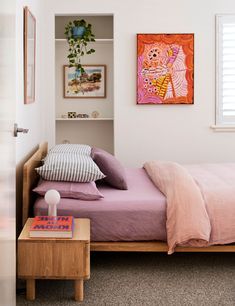 a bedroom with pink bedding and paintings on the wall above it's bed