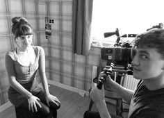 black and white photograph of a woman sitting on a chair with a camera in front of her