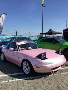 two pink and green cars are parked in a parking lot next to each other on the pavement