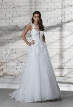 a woman in a white wedding dress standing next to a brick wall with her hands on her hips