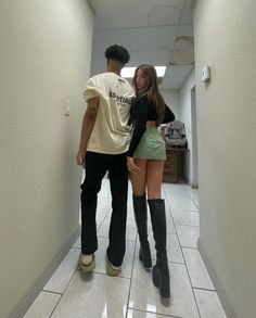 a man and woman are standing in an empty hallway, one is wearing black boots