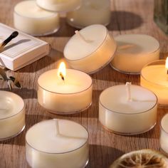 many lit candles sitting on top of a wooden table next to a slice of orange