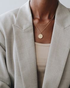 a woman wearing a jacket and necklace with a gold disc pendant on her left shoulder