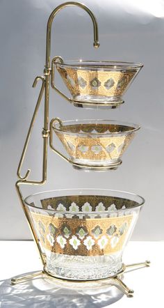 three glass bowls are stacked up on a metal stand with gold trimmings and decorative designs