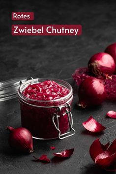 a jar filled with red onions sitting on top of a black table next to garlic