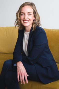 a woman sitting on top of a couch next to a yellow sofa cushion and smiling