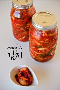 two jars filled with food sitting on top of a white table next to a spoon