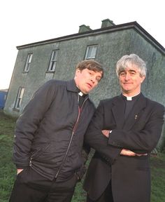 two men standing next to each other in front of a building with grass on the ground