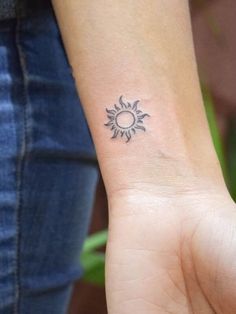 a woman's wrist with a small sun tattoo on the left side of her arm