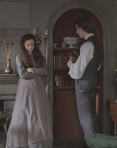 a man and woman standing next to each other in a room with bookshelves