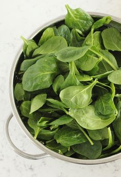 spinach leaves in a silver pot on a marble countertop, top view from above