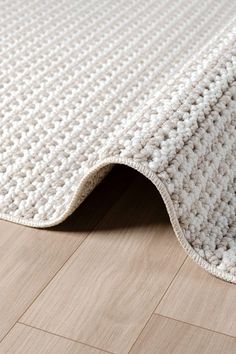 a white rug is laying on the floor next to a wooden floor with a light colored area rug