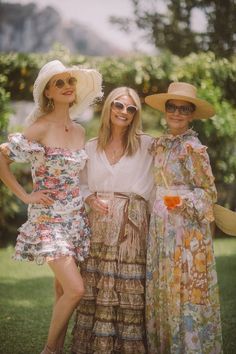 three women standing next to each other in dresses and hats