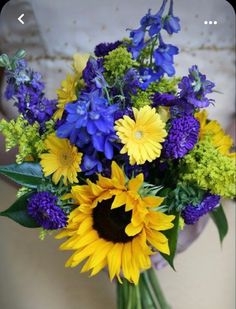 a bride holding a bouquet of sunflowers and blue flowers in her hands,