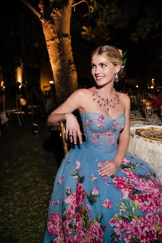 a woman sitting at a table wearing a blue dress with pink flowers on the skirt