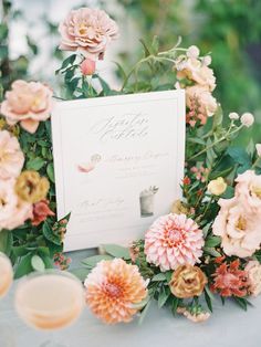 a table topped with flowers next to a white card and two glasses filled with champagne