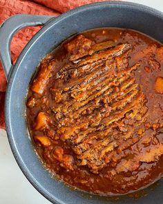 a pot filled with meat and sauce on top of a white countertop next to a red towel