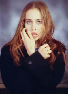 a woman with blue eyes and long hair posing for a photo in front of a gray background