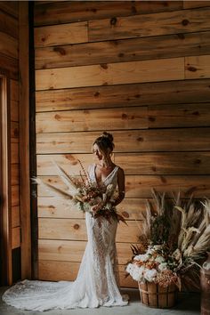 a woman standing in front of a wooden wall with flowers and feathers on the floor