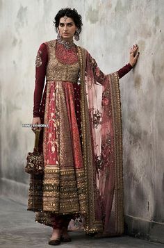 a woman in a red and gold dress standing next to a wall with her hands on her hips