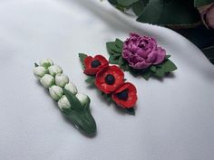 three different colored flowers are on a white cloth next to some green and pink flowers